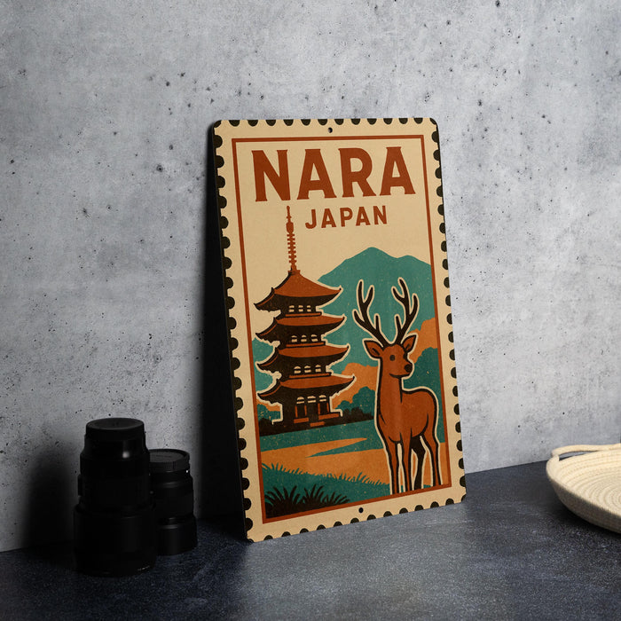 A vintage-style metal sign with the text "NARA JAPAN" and an illustration of a pagoda and a deer, placed on a gray countertop next to some black camera lenses.