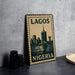 A metal sign with the text "LAGOS NIGERIA" and a graphic of a city skyline, placed on a table next to some black camera lenses.