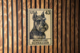 A miniature schnauzer dog stamp is displayed on a wooden wall.