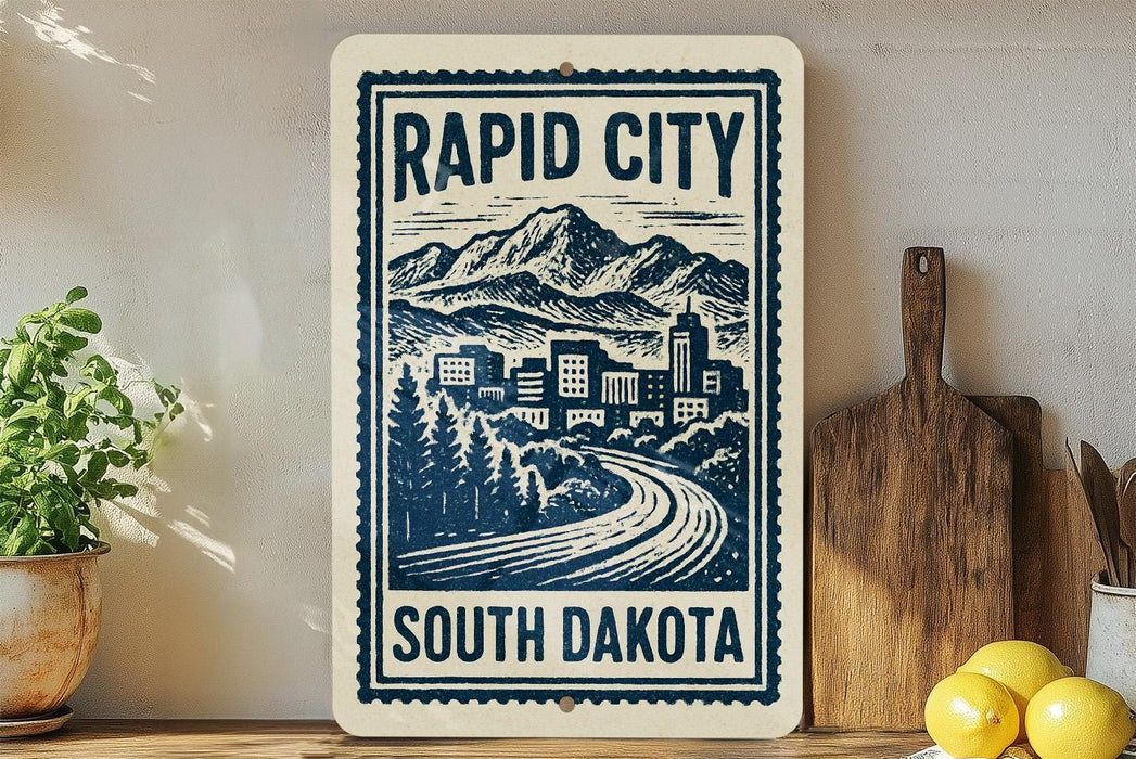 a sign for Rapid City, South Dakota, with a mountain landscape and a road leading to a city.