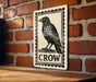 a black and white stamp-like sign with a black crow illustration on a brick wall.