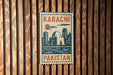 A vintage-style metal sign with the text "KARACHI PAKISTAN" displayed on a wooden wall.
