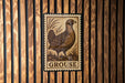 A metal sign with a bird illustration is mounted on a wooden wall.