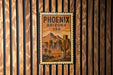 A vintage-style metal sign with the text "PHOENIX ARIZONA USA" displayed on a wooden wall.