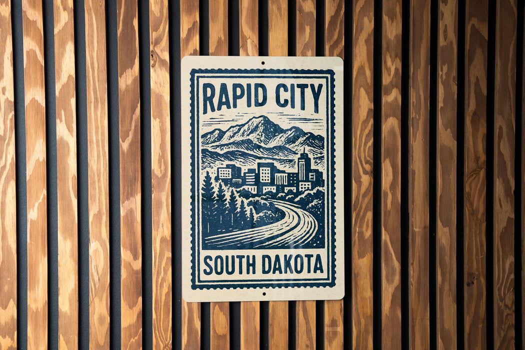 A sign for Rapid City, South Dakota, featuring a mountain landscape and a winding road.