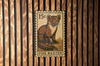 A 15 cent postage stamp featuring a pine marten, a small brown and white mammal, is affixed to a wooden wall.