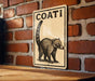 A sign with the word "COATI" on it is hanging on a brick wall.
