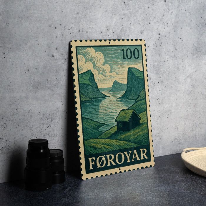 A metal stamp with a landscape scene depicting a house and mountains, placed on a table next to some black camera lenses.