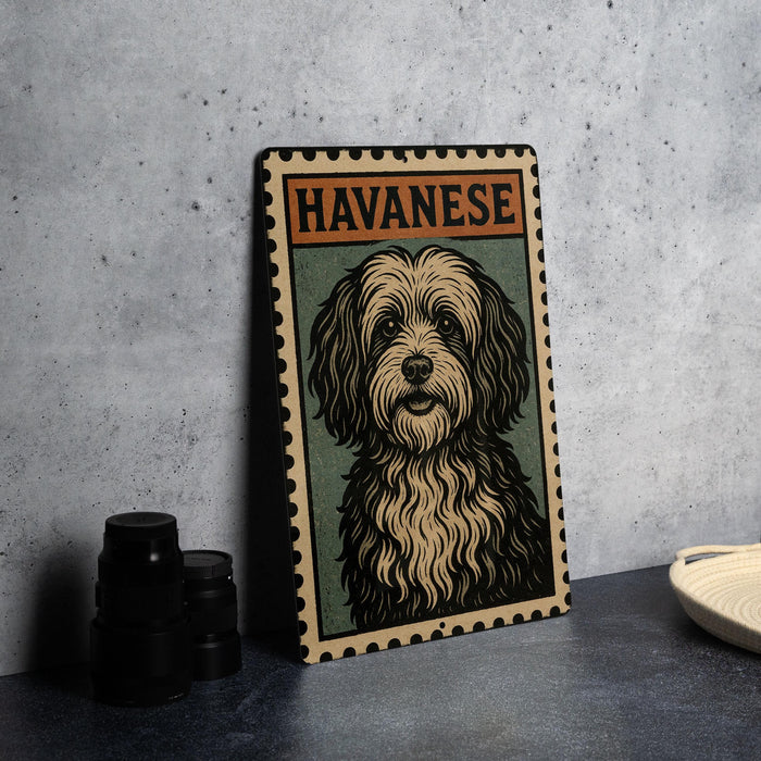 A metal sign with a stylized illustration of a dog, labeled "HAVANESE", is displayed on a table next to some black camera lenses.