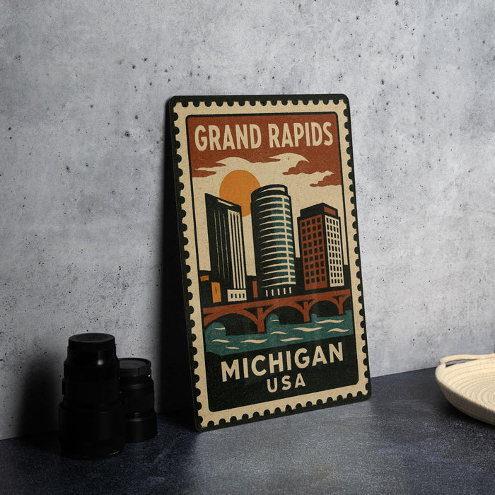 A vintage-style metal sign with a cityscape and the text "GRAND RAPIDS MICHIGAN USA" printed on it, placed on a gray countertop next to some black camera lenses.