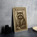 a wooden sign with a raccoon illustration on it, placed on a countertop next to some black camera lenses.