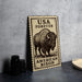A metal sign with a bison illustration and text, placed on a table next to some black camera lenses.