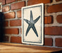 a wooden table with a framed picture of a starfish hanging on the wall behind it.