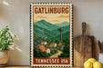 A vintage-style metal sign with the text "GATLINBURG TENNESSEE USA" and an illustration of a mountain town with a tower, surrounded by trees and houses.