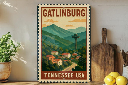A vintage-style metal sign with the text "GATLINBURG TENNESSEE USA" and an illustration of a mountain town with a tower, surrounded by trees and houses.