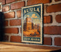 A vintage-style metal sign with the text "AL-ULA SAUDI ARABIA" displayed on a brick wall.
