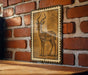 a wooden table with a framed illustration of a gazelle or antelope on it, mounted on a brick wall.