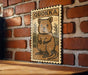A wooden table with a framed illustration of a quokka, a small marsupial, on a brick wall.