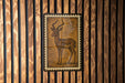 a wooden wall with a framed illustration of a gazelle or antelope, which appears to be a decorative piece.