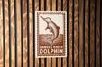 A sign with a dolphin illustration and the text "Ganges River Dolphin" is displayed on a wooden wall.