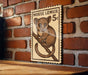 A wooden table with a brick wall in the background, and a framed image of a brown mouse on a branch hanging on the wall.