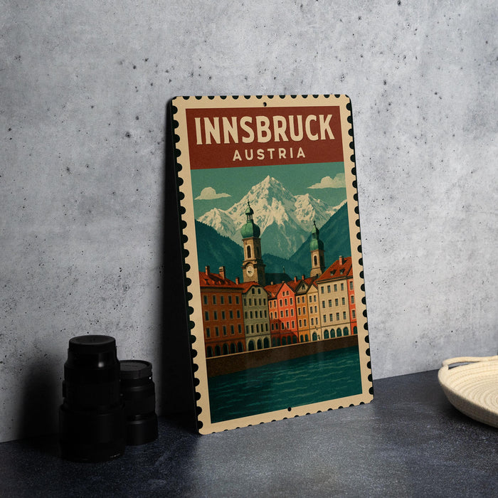 A vintage-style metal sign with the text "INNSBRUCK AUSTRIA" and an illustration of a cityscape with mountains in the background.