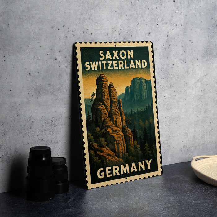 A metal stamp depicting Saxon Switzerland, with a mountain landscape and text indicating the location.