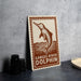 a sign with a dolphin illustration and the text "Ganges River Dolphin" on it, placed on a table next to some black camera lenses.