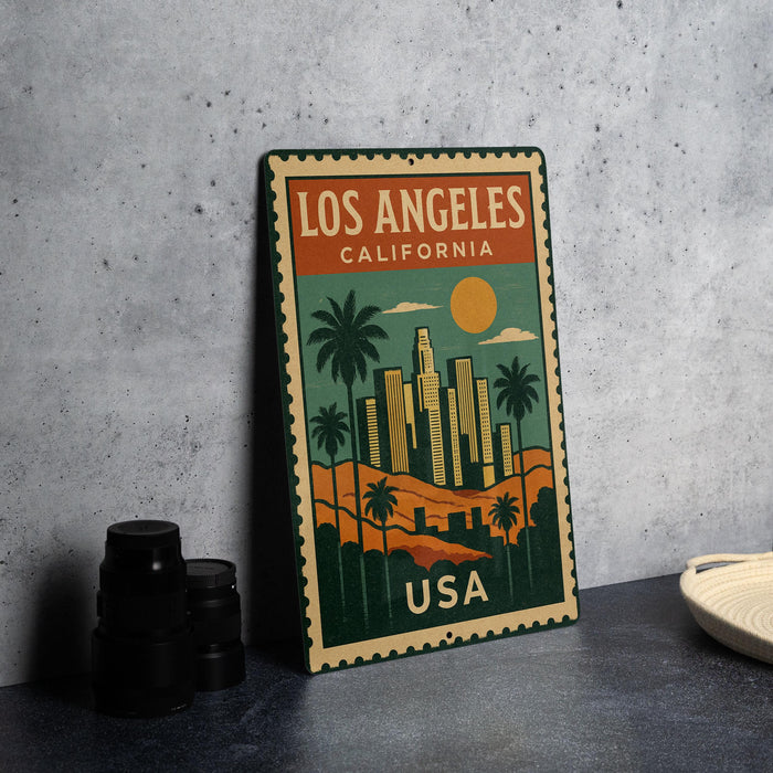 A vintage-style metal sign with a colorful illustration of Los Angeles, California, featuring palm trees, skyscrapers, and a sun.