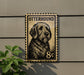 A metal sign featuring a dog's portrait, mounted on a wall next to a plant.