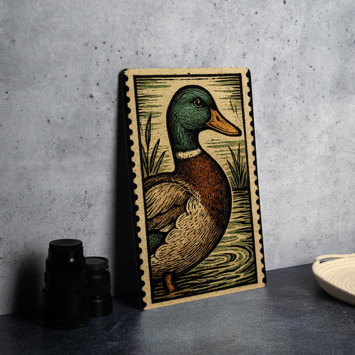 A framed illustration of a duck is displayed on a table, with a stack of black camera lenses and a white dish visible to the side.