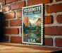A vintage-style postage stamp depicting Yosemite National Park, featuring a scenic landscape with mountains, a river, and a wooden bench.