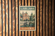 A vintage postage stamp from Slovenia featuring a cityscape with a bridge and church, mounted on a wooden wall.