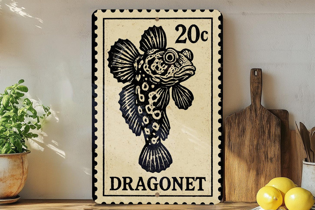 A 20c postage stamp featuring a black and white illustration of a dragonnet fish, placed on a wooden surface next to a wooden cutting board and a potted plant.