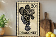 A 20c postage stamp featuring a black and white illustration of a dragonnet fish, placed on a wooden surface next to a wooden cutting board and a potted plant.