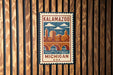 A vintage-style metal sign with a cityscape and a bridge, mounted on a wooden wall.