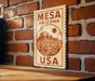 A wooden sign with the text "MESA ARIZONA USA" is displayed on a brick wall.