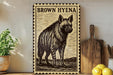 a framed illustration of a hyena, a type of wild dog, on a wooden surface.