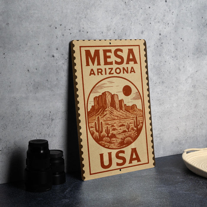 A vintage-style metal sign with the text "Mesa Arizona USA" printed on it, featuring an illustration of a desert landscape with mountains and cacti.