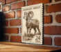 A wooden table with a large, detailed, engraved stamp featuring a bighorn sheep on it, mounted on a brick wall.