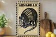 A metal sign with the word "ARMADillo" on it, featuring a detailed illustration of an armadillo. The sign is displayed on a shelf next to a wooden cutting board and a potted plant.