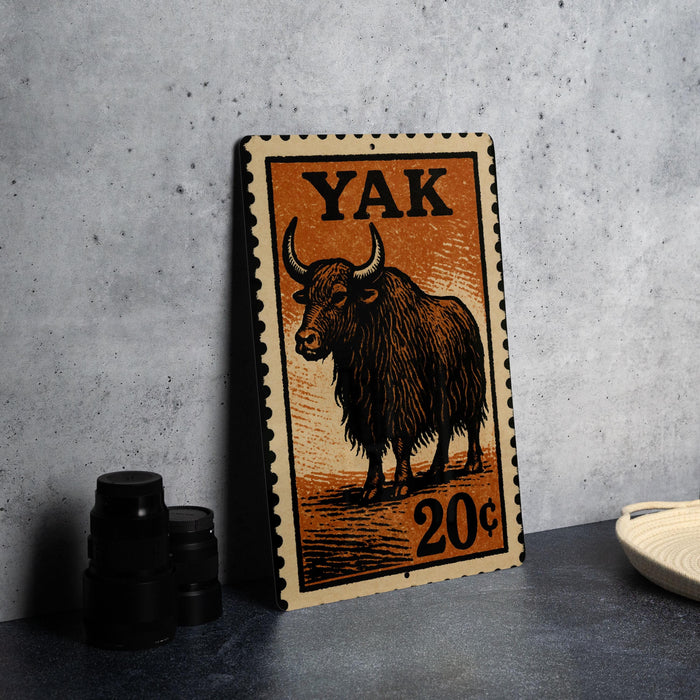 A metal sign with an illustration of a yak and the text "YAK" and "20¢" printed on it, placed on a gray surface next to some black camera lenses.
