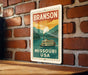 A vintage-style metal sign with the text "BRANSON MISSOURI USA" and an illustration of a steamboat on a river.