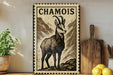 a decorative metal sign with a printed illustration of a mountain goat, placed on a wooden surface next to a wooden cutting board and some lemons.
