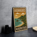 A vintage-style metal sign with the text "RODRIGUEZ MAURITIUS" and an illustration of a coastal landscape with mountains, water, and clouds.