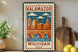 A vintage-style metal sign with a cityscape illustration and the text "KALAMAZOO MICHIGAN USA" is displayed on a shelf next to a wooden cutting board and a potted plant.