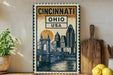a decorative metal sign with a cityscape and a bridge, placed on a wooden surface next to a wooden cutting board and some lemons.