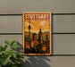 A vintage-style metal sign with the word "STUTTGART" displayed prominently, featuring a cityscape with a clock tower and other architectural elements.