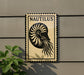 a sign with the word "Nautilus" on it, mounted on a wall next to a plant.