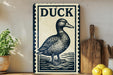 a decorative sign with a duck illustration, placed on a wooden surface next to a wooden cutting board and some lemons.